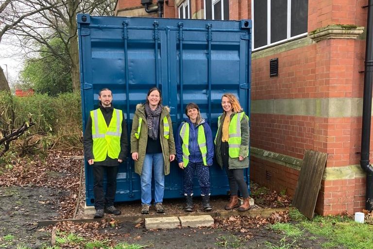 A photo of four of the MCRLOT team, standing in front of a blue shipping container wearing hi-vis vests
